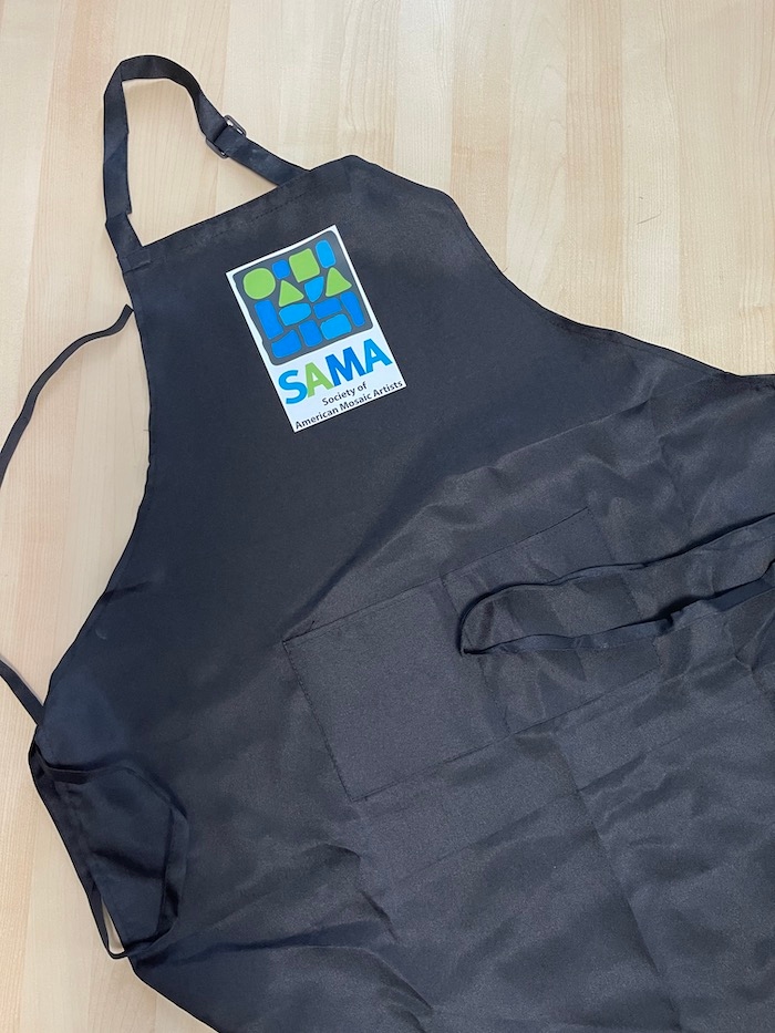 Product Description: Black Studio Apron with twofront pockets, adjustable halter neck and tie waist is embroidered with SAMA'scolorful logo.</br></br>100% polyester.</br></br>33" from top of bib to bottom front.</br></br>26.5" wide</br> SAMA Logo Apron